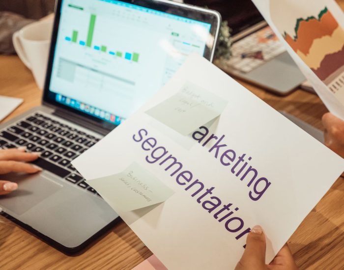 A modern workspace showing hands analyzing marketing data on a laptop and paper documents.